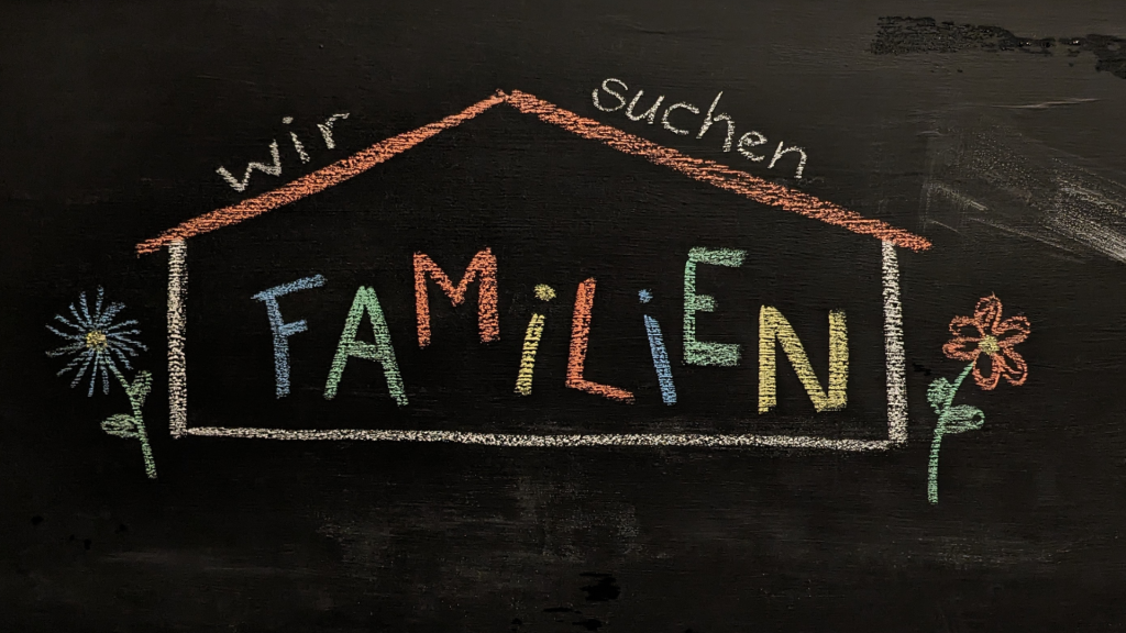 Symbolbild: Wir suchen Familien bunt geschrieben in ein gezeichnetes Haus.