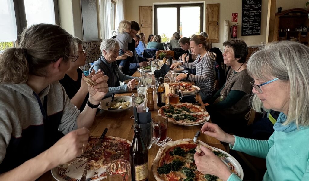Eine Gruppe, Gesellschafter und Interessenten, sitzen am Tisch und essen Pizza.
